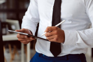 Homem de gravata de pé, com tablet à mão dando chekc e lista de tarefas documentação